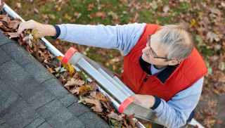Man standing on ladder cleaning leaves from gutter