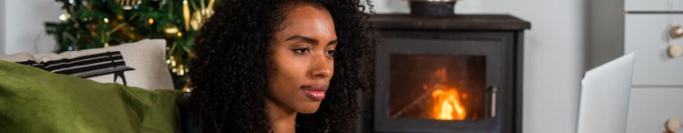 A woman using a laptop at home next to a fireplace.