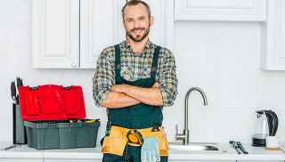 A plumber standing and smiling with his tools in front of the kitchen sink