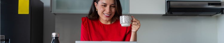 woman wearing red working on laptop at home while drinking coffee