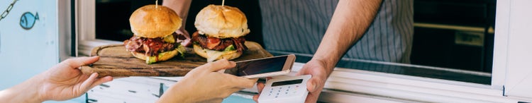 woman buying burgers from food van and using smartphone