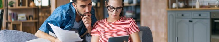 man and woman on couch concentrating on paper and computer
