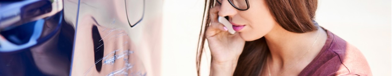 Woman on the phone while inspecting scratch on her car 