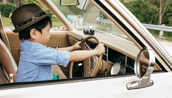 Boy pretending to drive in a vintage car