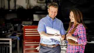 Mechanic holding a notepad discusses with woman