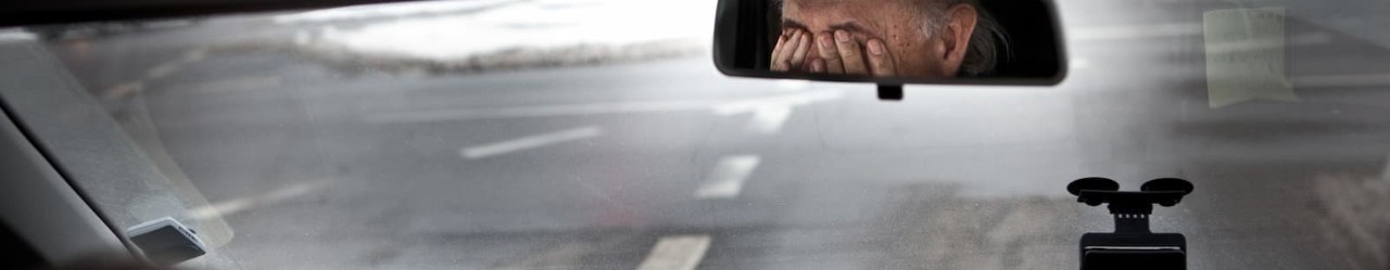 Tired man rubbing eyes in rearview mirror