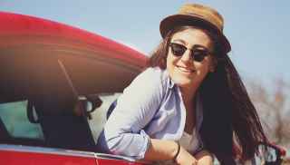 Woman leaning out of car window wearing a hat and sunglasses