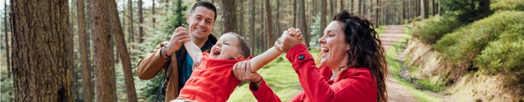 parent swinging child in air in forest while walking