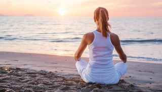 Woman meditating on beach facing the sunset