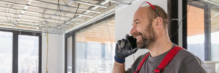 Tradesman on construction site placing his mobile phone to his ear and smiling.