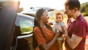Smiling couple stand beside their car in nature on a sunny day