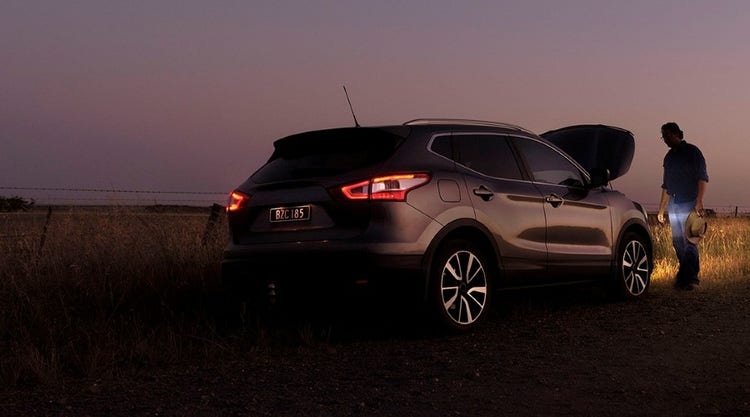 Man standing beside car broken down by a country road at twilight