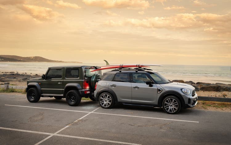 Two cars parked at a beach, one with surfboards on the roof