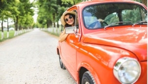 Woman driving vintage orange car in the countryside with her head out the window