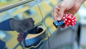 Hand holding car keys with a gift ribbon next to car door