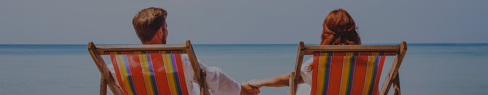 Couple holding hands sitting on deck chairs at the beach