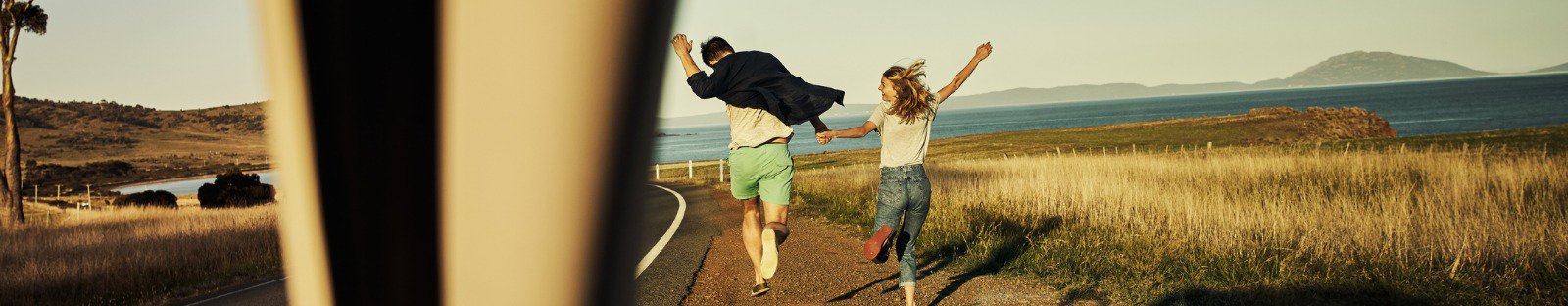 Couple running to beach in front of parked car 
