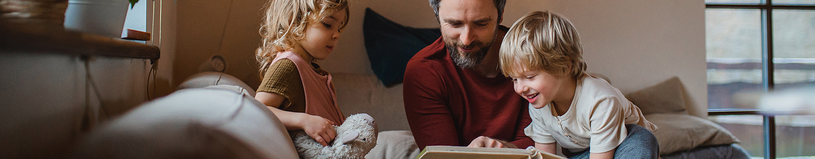 Mature father with two small children resting indoors at home, looking at photo album.