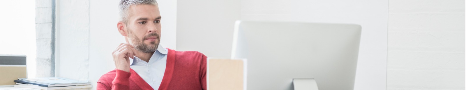 Man in red jumper looking at desktop screen