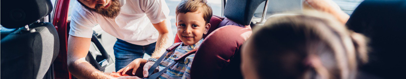 Man putting seatbelts on kids in car 
