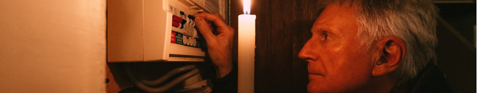 Senior man checking home fuse box by candlelight during power outage