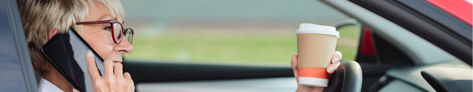 smiling mature woman talking on the phone and holding a cup of coffee while driving