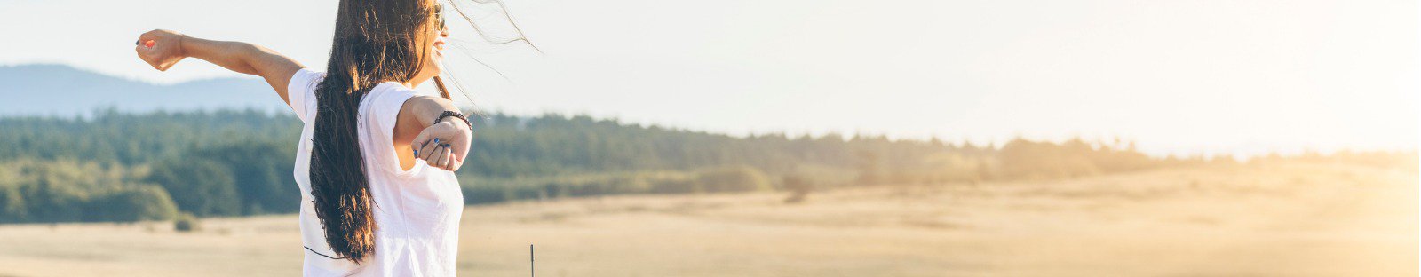 Smiling woman standing next to car with arms outstretched