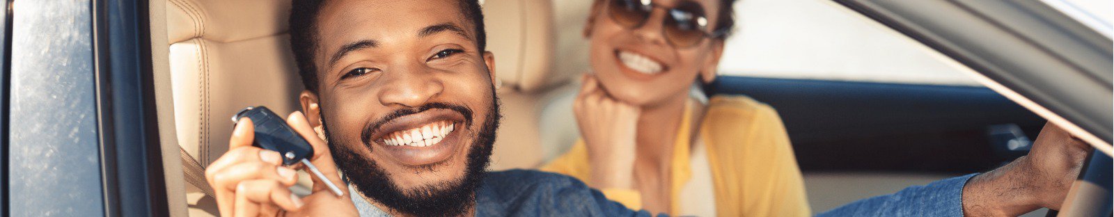 Smiling young man holding keys in car drivers seat