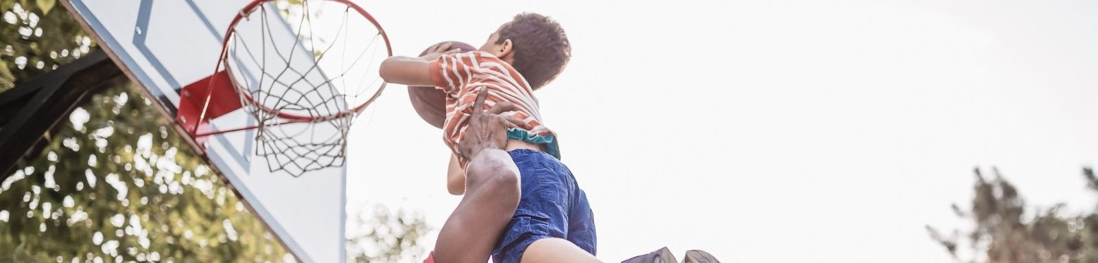 Father lifting young son up to basketball hoop for a dunk