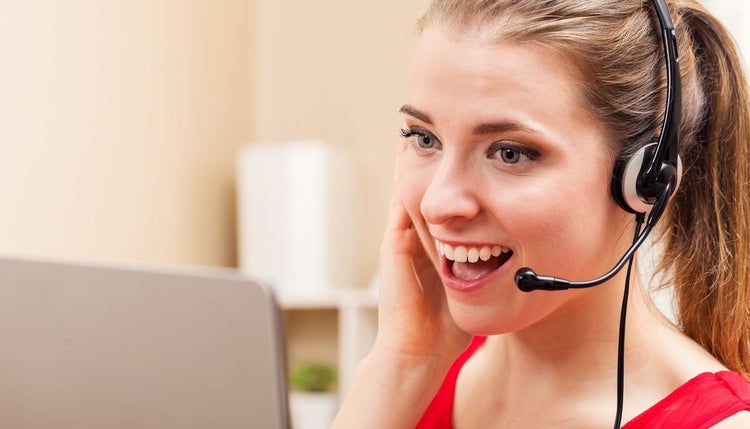Woman sitting at computer is talking on a headset and smiling