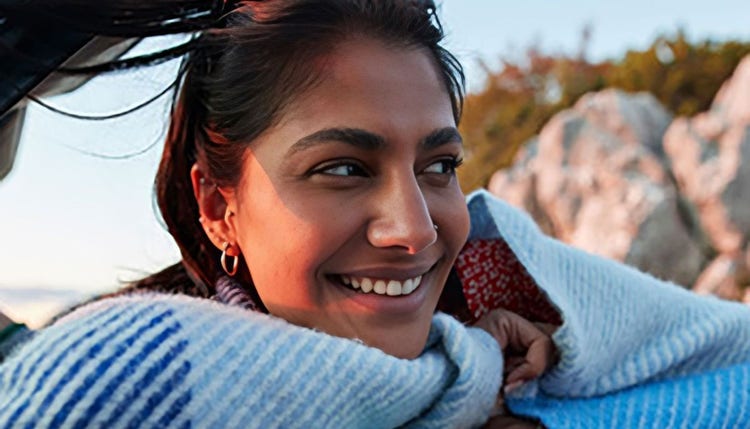 Woman wearing a blue woolen shawl is smiling as she leans on a blue car