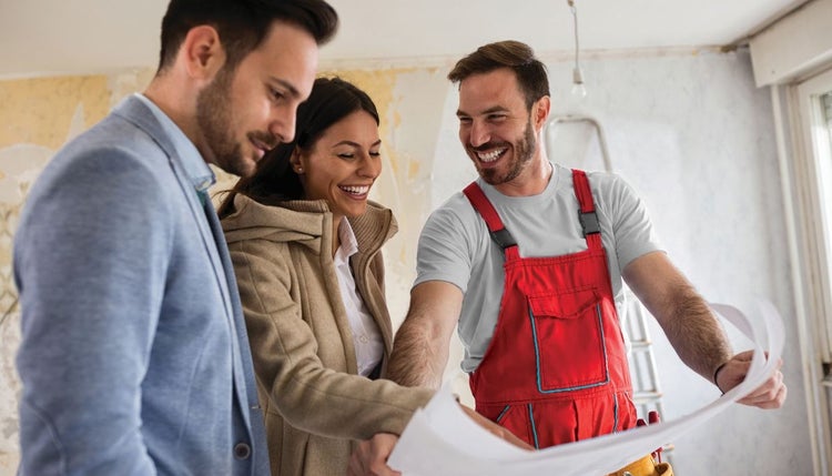 Tradie wearing red overalls inside house being rebuilt, showing smiling couple plans
