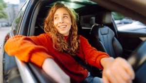 Young woman in an orange jumper driving a car and smiling