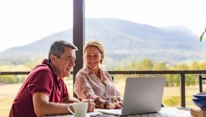 Couple using a laptop on porch with mountains in the background