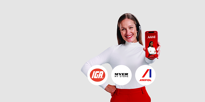 Professional woman holding out smartphone showing AAMI App screen. The IGA, Myer and Ampol logos are in front of her.